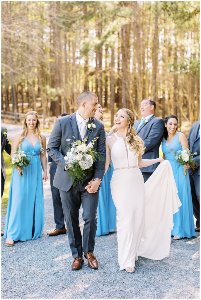 The wedding party walks down a gravel pathway laughing.