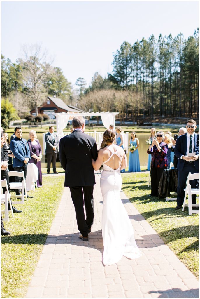 Image of the back of the bride's dress walking down the aisle with her father.