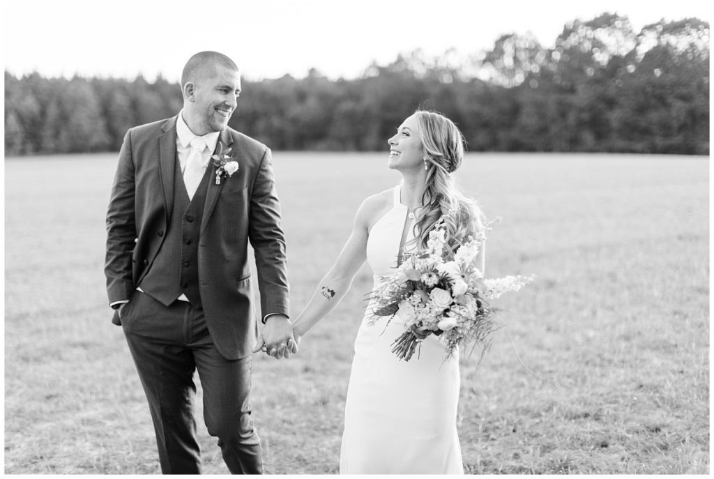 Black and white image of the bride and groom walking through a field.