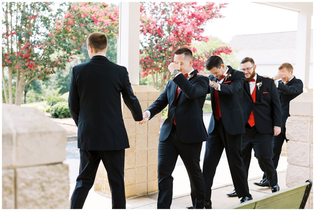The groom leads the groomsmen out with their eyes closed to see the bride for the first time.