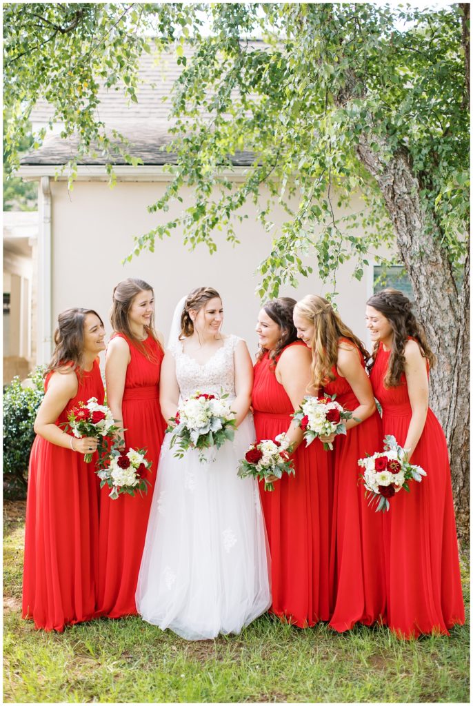 The bridesmaids laugh together showing off their red dresses and bouquets.