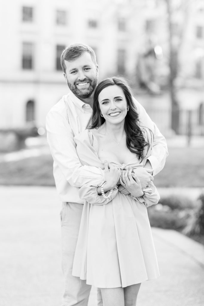 A black and white engagement portrait of Scott hugging Jessica in downtown Raleigh | Raleigh NC Wedding Photographer