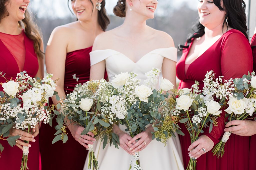 The bridesmaids wore red dresses in a variety of styles with white bouquets of roses and baby's breath| Raleigh Wedding Photographer