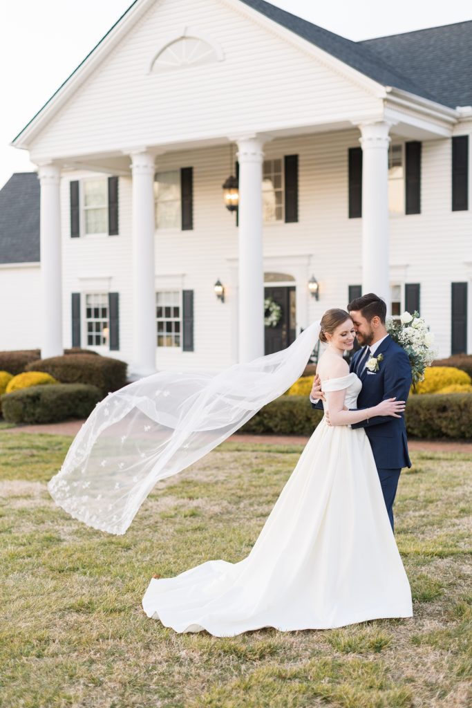 The bride and groom in front of Seven Paths Manor as her veil flies through the wind | Raleigh Wedding Photographer