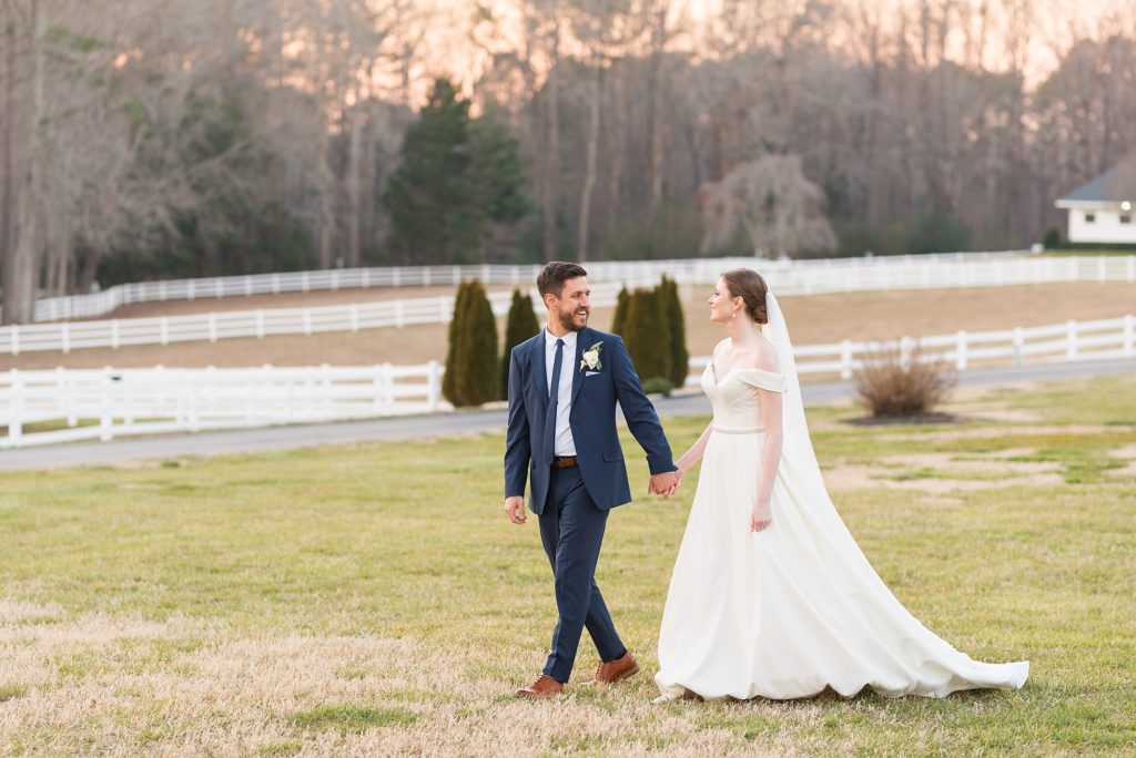 The bride and groom walk through a field holding hands | Raleigh Wedding Photographer