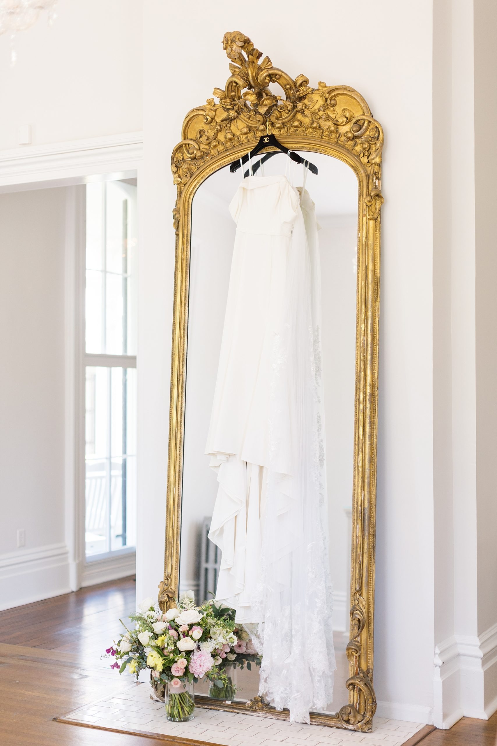 Bridal gown hanging on a Chanel hanger on a gold ornate mirror | Merrimon Wynne Wedding | Sarah Hinckley Photography | Raleigh NC Wedding Photographer