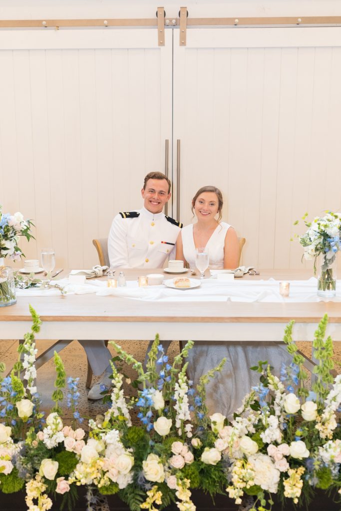 The bride and groom together at their head table surrounded by blue and white flowers | Carolina Grove | Raleigh NC Wedding Photographer | Sarah Hinckley Photography