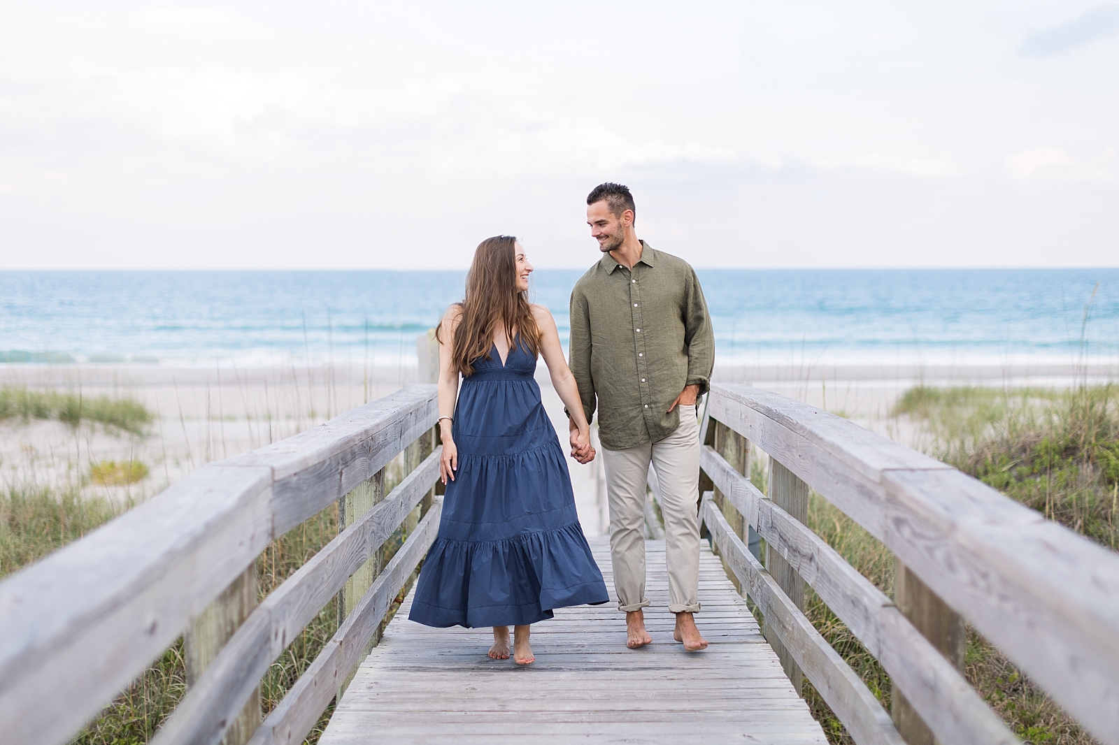 Maddie and Dylan hold hands and walk along the boardwalk at Topsail Beach | Raleigh North Carolina Wedding Photographer