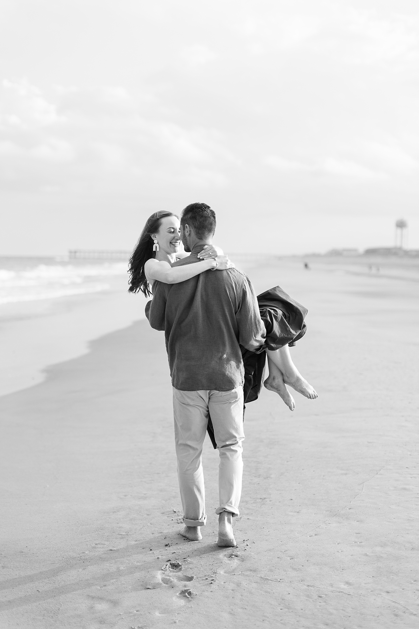 Black and white photo of Dylan carrying Maddie off along the beach | Raleigh North Carolina Wedding Photographer