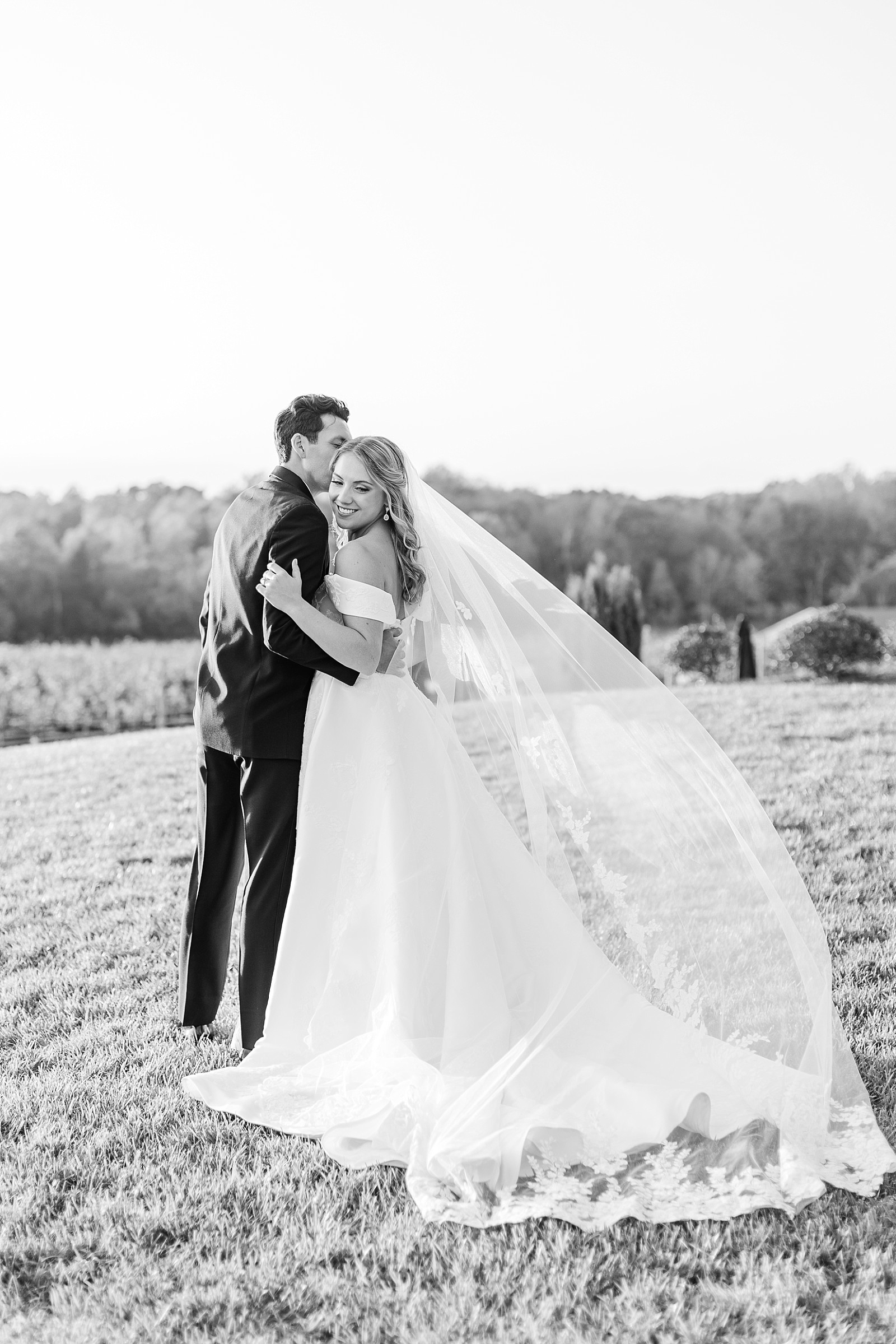 black and white photo of bride and groom with bride's veil blowing. in the wind