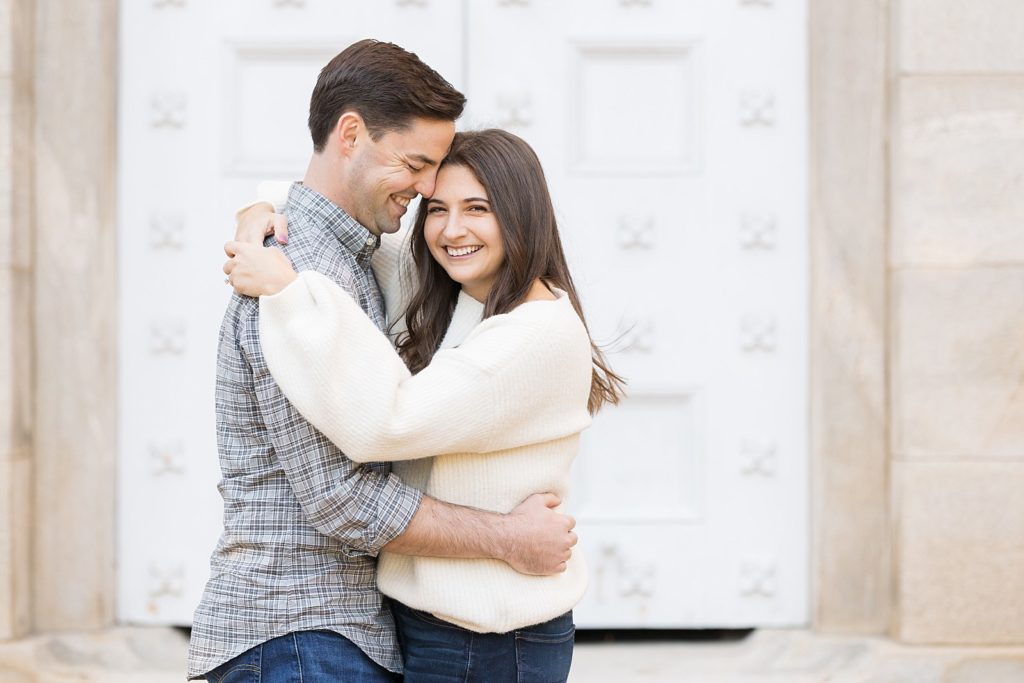 Couple embracing in front of white iron door | Downtown Raleigh Engagement Photoshoot | Raleigh NC Wedding & Engagement Photographer | Sarah Hinckley Photography 