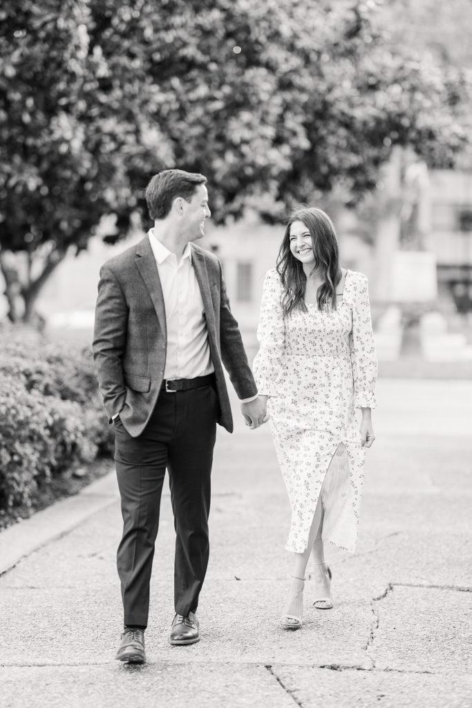 black and white photo of couple smiling at each other while walking | Downtown Raleigh Engagement Photoshoot | Raleigh NC Wedding & Engagement Photographer | Sarah Hinckley Photography 
