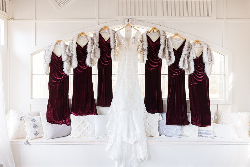 Red Velvet bridesmaids dresses hanging in the window with wedding dress | Christmas Wedding at Pinehill Pavilion | Raleigh NC Wedding Photographer 