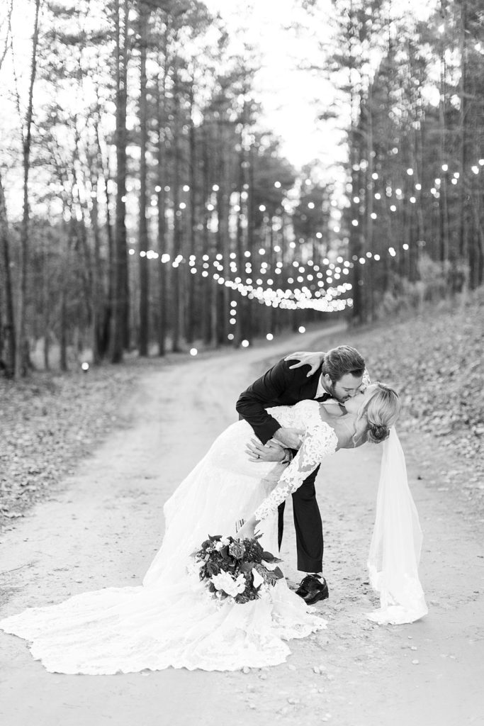 Black and white photo Bride and groom kissing in front of lights | Christmas Wedding at Pinehill Pavilion | Raleigh NC Wedding Photographer 