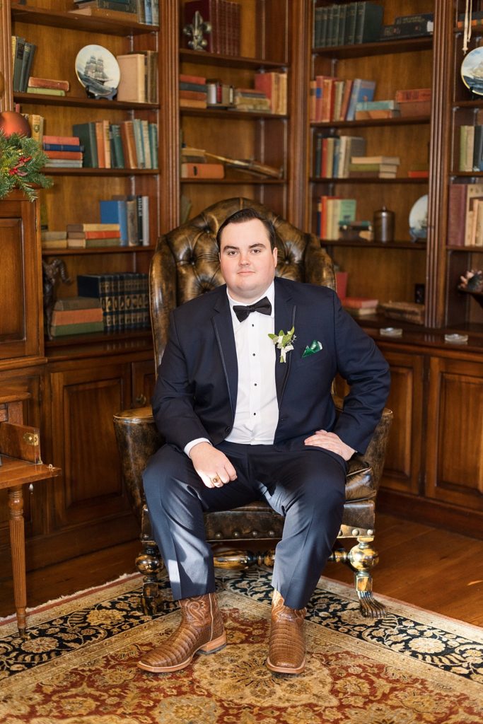 Groom sitting in leather chair in library | Emerald Christmas Wedding at The Sutherland Estate | Raleigh NC Wedding Photographer