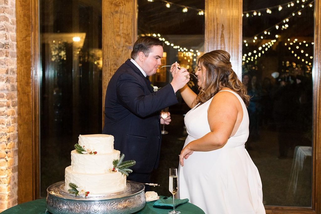 Bride and groom feeding each other wedding cake | Emerald Christmas Wedding at The Sutherland Estate | Raleigh NC Wedding Photographer