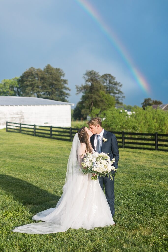 Bride and groom kissing outside with a rainbow in background | Amazing Graze Barn Wedding | Amazing Graze Barn Wedding Photographer
