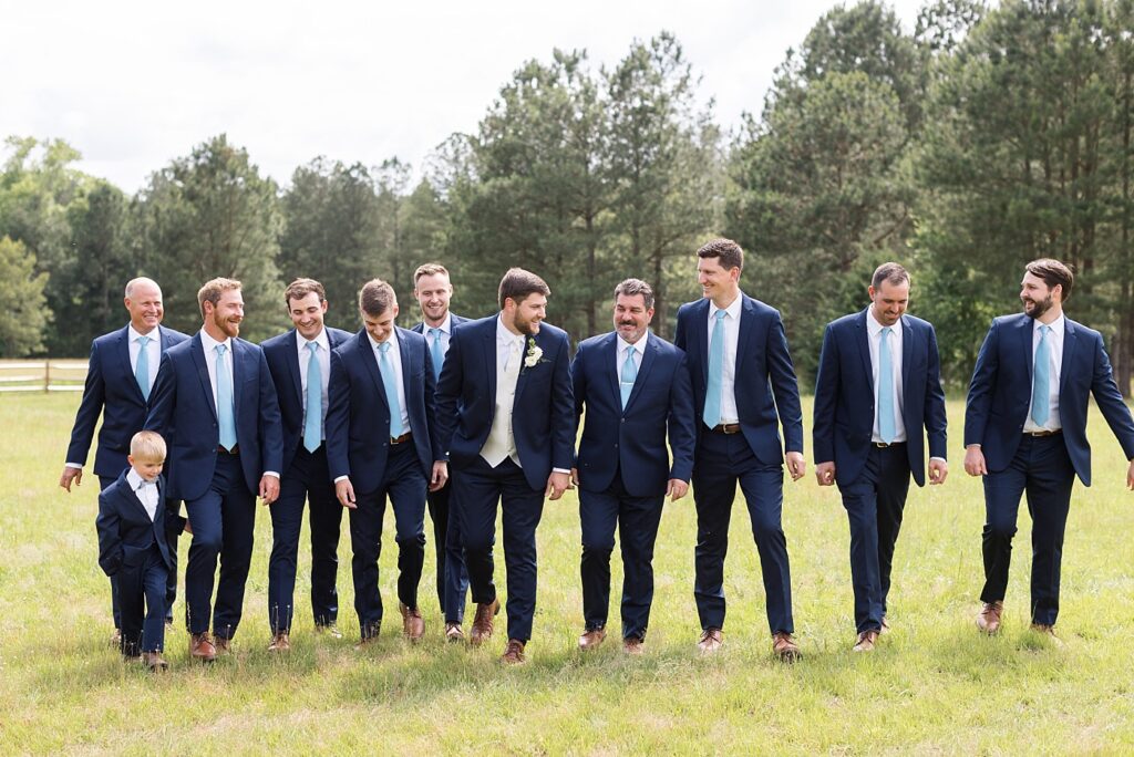 Groom walking with groomsmen in field outside venue | The Evermore Wedding | The Evermore Wedding Photographer | Raleigh NC Wedding Photographer