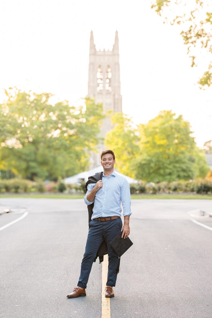 Grad student holding graduation gown over shoulder and smiling in front of Duke Chapel | Duke University Grad | Durham Senior Photographer