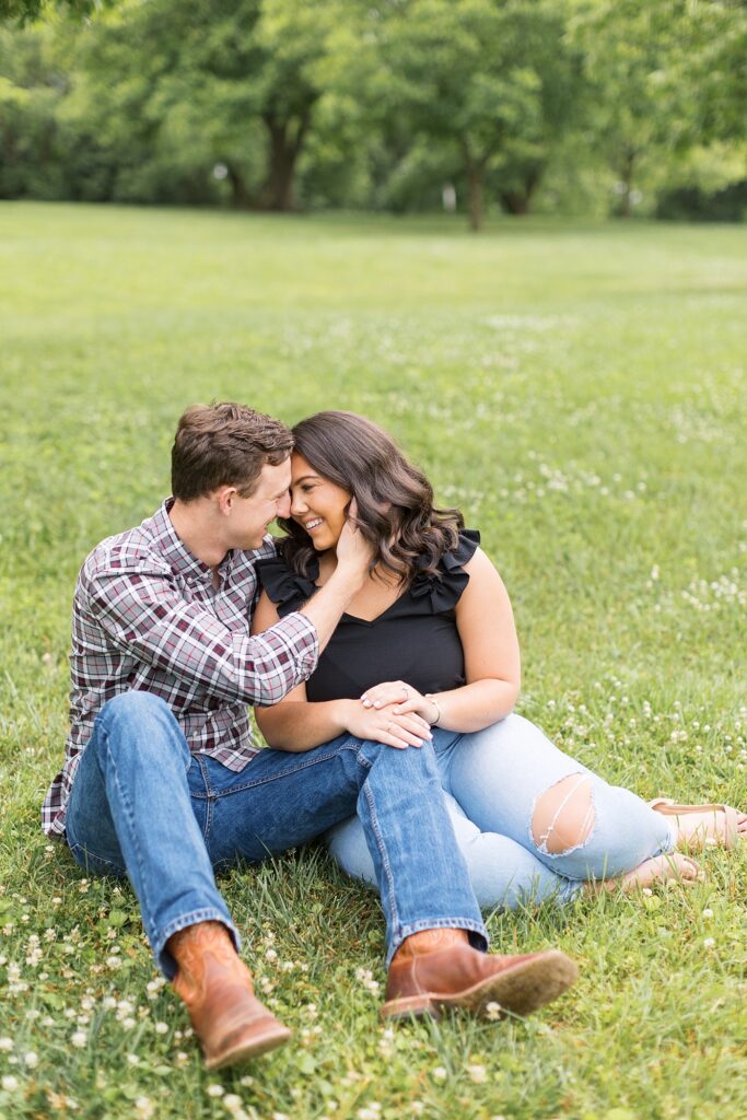 Couple sitting on grass in open field while staring at each other's eyes | Raleigh NC Engagement Photographer | Historic Oak View Engagement Session