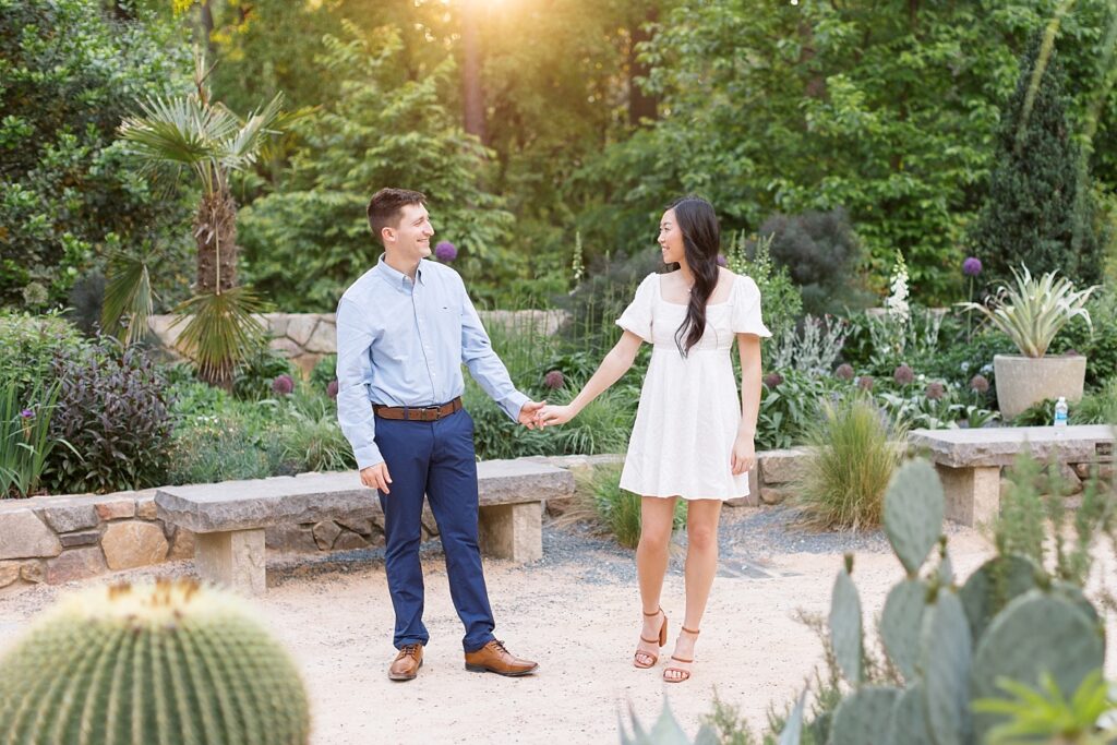 Couple holding hands in garden by bench | Duke Gardens engagement photos | Raleigh NC wedding photographer 
