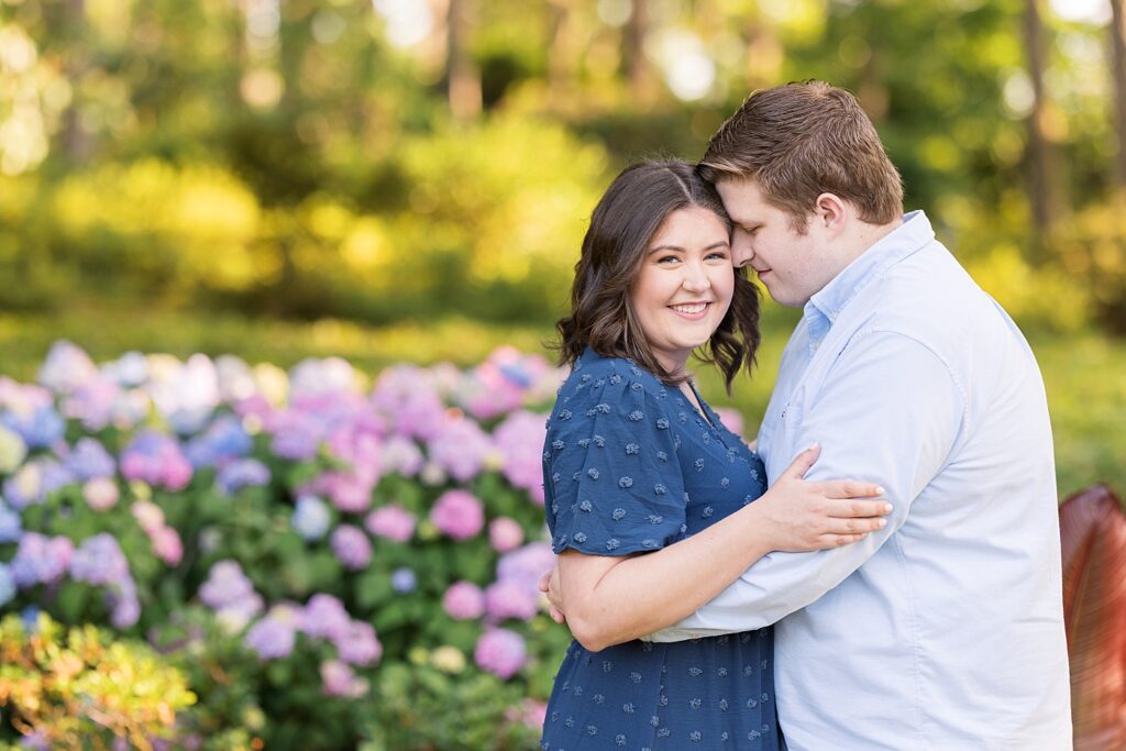 Couple embracing in garden with colorful pink and blue flowers | WRAL Gardens engagement photos | Raleigh NC wedding photographer 