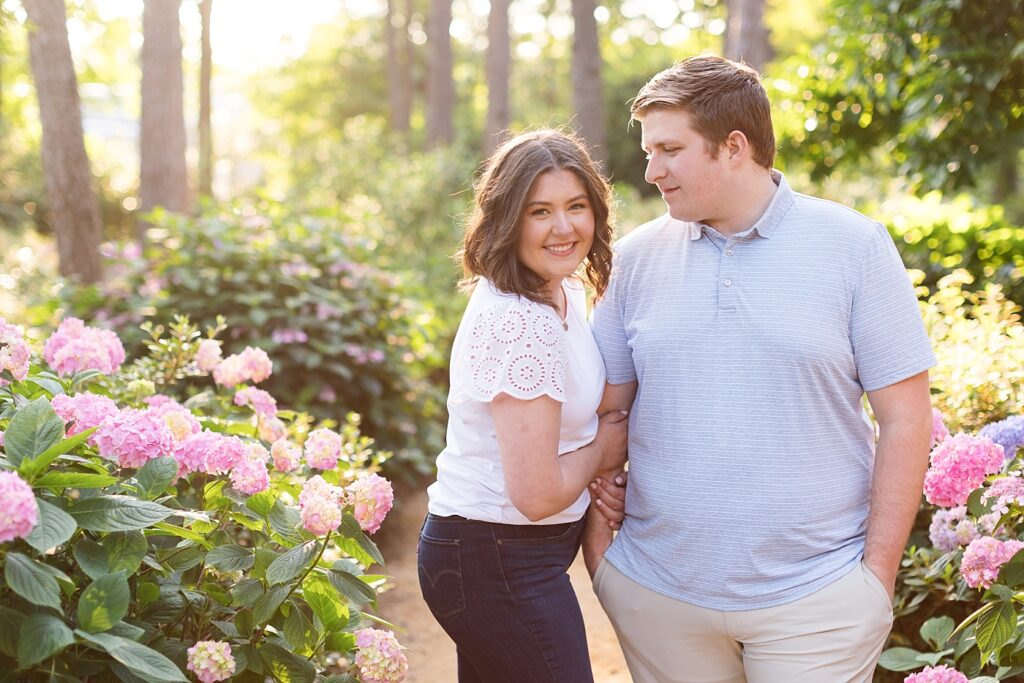 Couple embracing in garden with pink flowers | WRAL Gardens engagement photos | Raleigh NC wedding photographer 