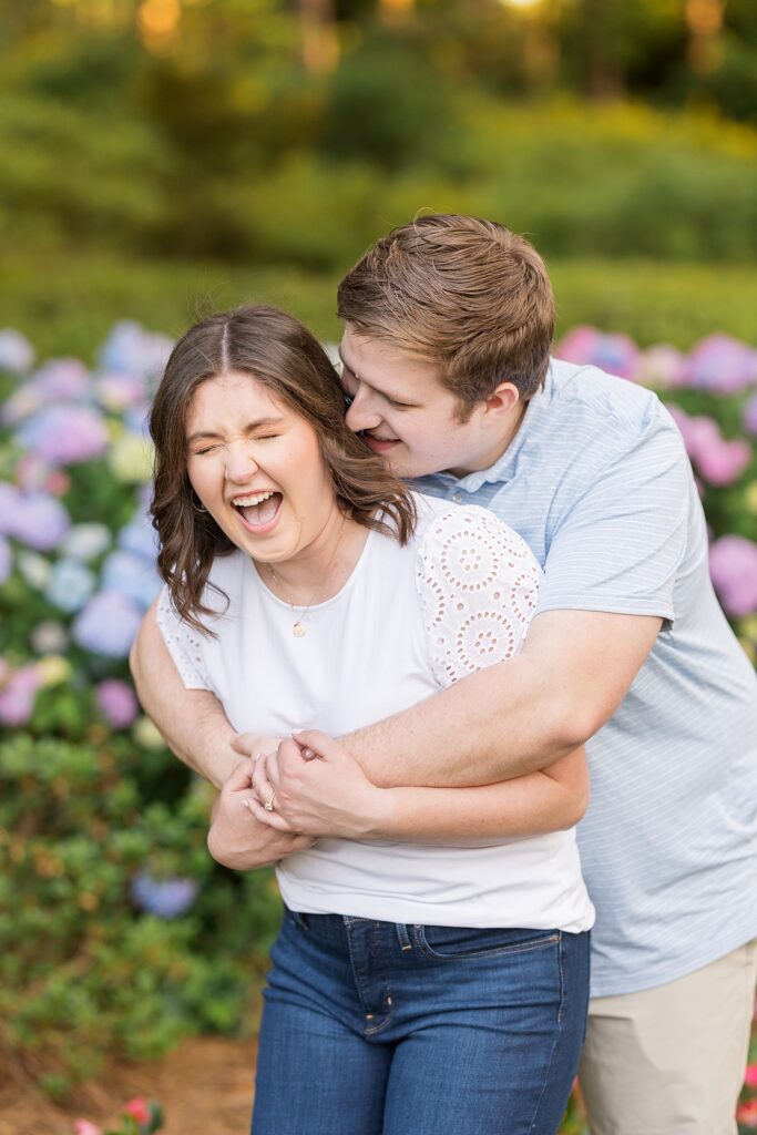 Couple embracing in garden with colorful pink and blue flowers | WRAL Gardens engagement photos | Raleigh NC wedding photographer 