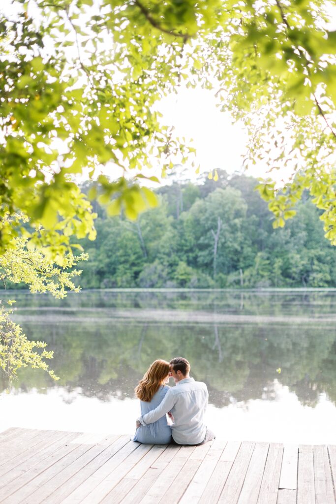 Couple sitting on dock and staring at each other by lake | Yates Mill engagement photos | Raleigh NC wedding photographer 