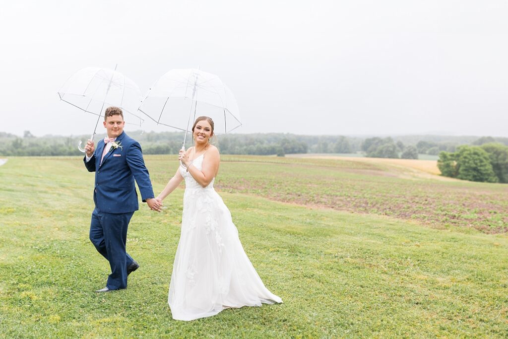 Bride and groom holding hands on field holding an umbrella | Rainy wedding | Rustic wedding | Harvest House Wedding | Harvest House Photographer | Raleigh NC Wedding Photographer