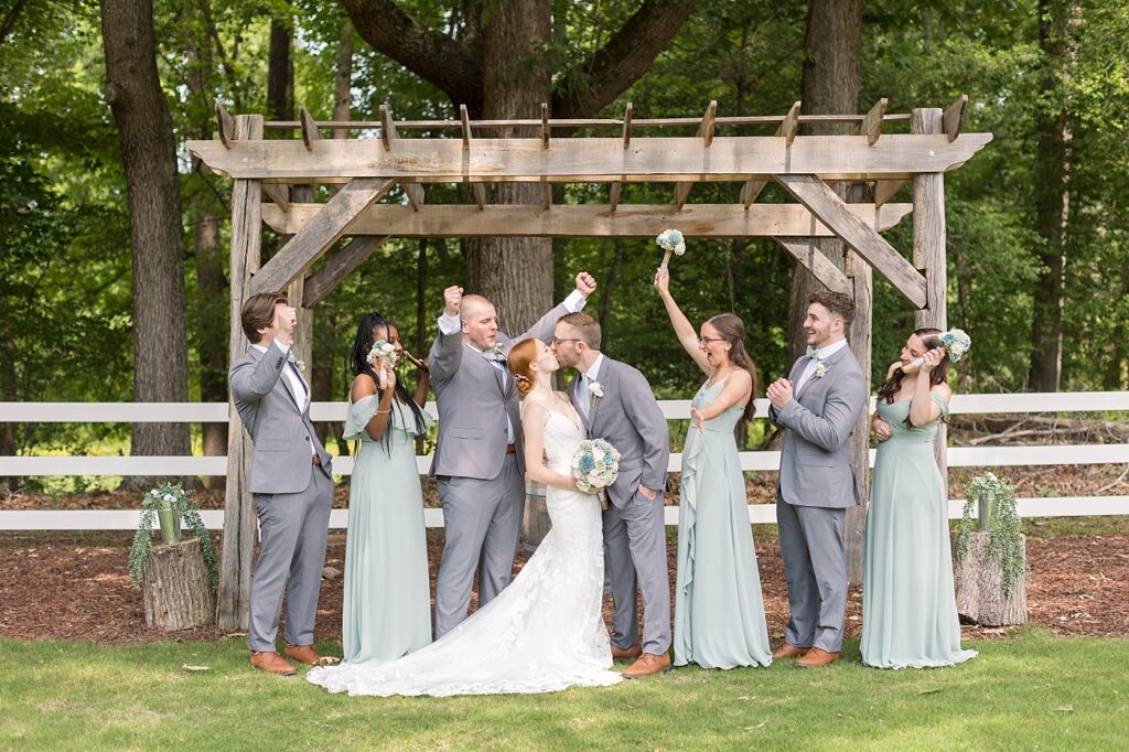 Bride and groom kissing while wedding party cheers | Rustic Wedding | Twin Oaks Barn Wedding | Twin Oaks Barn Wedding Photographer | Raleigh NC Wedding Photographer