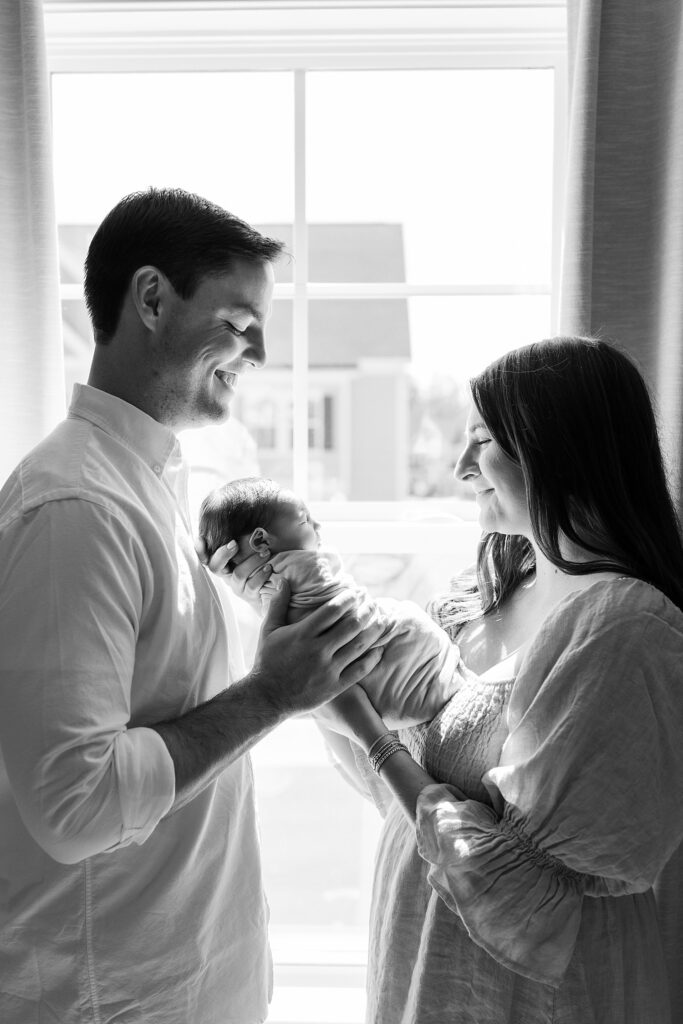 sleeping swaddled baby | baby girl with bow | new parents holding baby | lifestyle newborn photos | in-home newborn session | newborn photography Raleigh NC | Raleigh newborn photographer